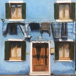 Blue three storey building with laundry hanging across the front of the second storey. The building has a brown door and the windows have dark green shutters.