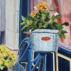 A bike leans against the side of building with a window. It has a white basket with flowers in it. There are two pots of flowers on the ground on either side of the window.