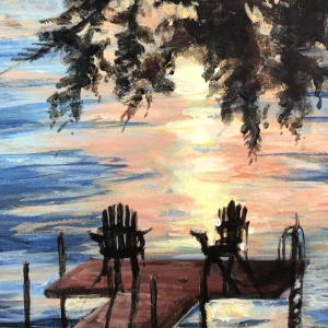 Muskoka chairs sit on a dock facing towards a lake. The setting sun highlights the water with warm pinks and yellows.