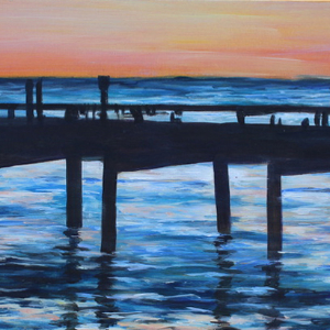 Silhouette of a Pier in Mexico during a sunset. The pink and yellow tones of the sky are light reflected in the foreground water.